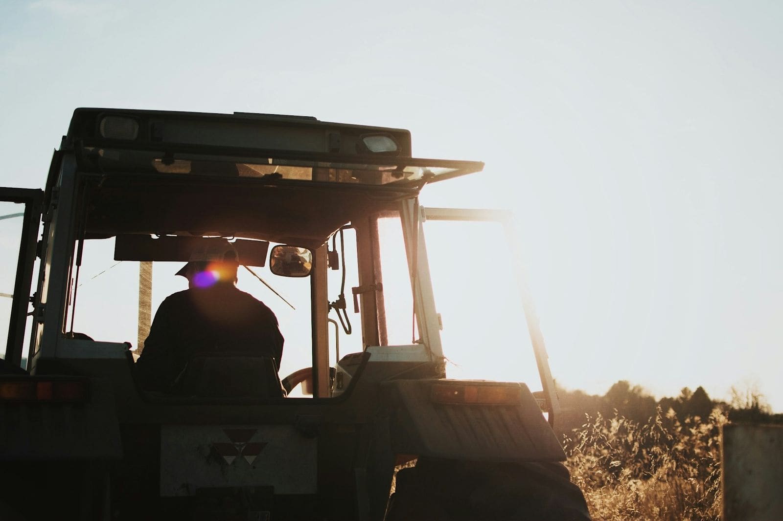 Silhuett av bonde på traktor i solnedgang